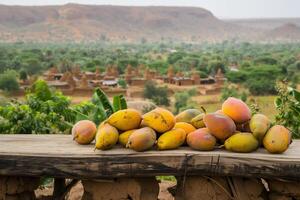 ai generado Fresco mali mangos en un de madera mesa con el dramático paisaje de africano pueblo y montañas en el antecedentes foto