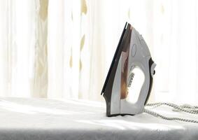 White iron on an Ironing Board against a window background. photo