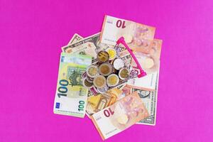 Mini shopping basket with coins and paper Euro and dollar bills on a pink background. Finance and the concept of saving money photo
