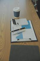 Close up view of simple workspace with laptop, notebooks, coffee cup and tree pot on white table with blurred office room background photo