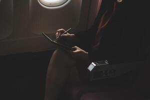 Blonde female tourist checking incoming notification on smartphone sitting on seat of airplane with netbook.Young businesswoman share media from telephone on laptop computer during plane flight photo