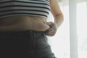 mujer cuerpo grasa barriga. obeso mujer mano participación excesivo barriga gordo. dieta estilo de vida concepto a reducir barriga y forma arriba sano estómago músculo. foto