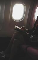 Blonde female tourist checking incoming notification on smartphone sitting on seat of airplane with netbook.Young businesswoman share media from telephone on laptop computer during plane flight photo