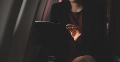 Blonde female tourist checking incoming notification on smartphone sitting on seat of airplane with netbook.Young businesswoman share media from telephone on laptop computer during plane flight photo