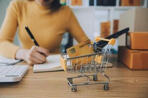 mujer joven dueña de una pequeña empresa comprando en línea en casa. tomando nota de los pedidos de los clientes con teléfonos móviles. pyme emprendedor o concepto de estilo de vida independiente. foto