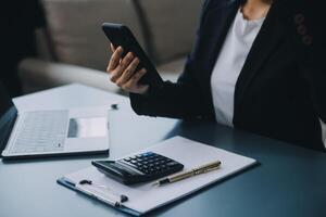 Hispano mujer de negocios en formal atuendo en su oficina contento y alegre mientras utilizando teléfonos inteligentes y laboral. joven mujer de negocios utilizando aplicaciones en célula Los telefonos, leyendo noticias, rápido conexión foto