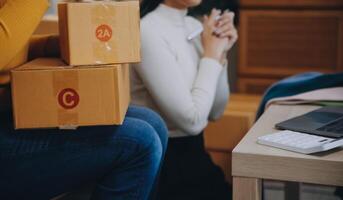 Las pymes asiáticas usan computadoras portátiles para verificar las cajas de envío en línea de pedidos de clientes en casa. Emprendedor de pequeñas empresas pyme freelance. negocio en línea, concepto de trabajo en casa. foto