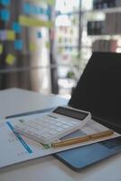 Close up view of simple workspace with laptop, notebooks, coffee cup and tree pot on white table with blurred office room background photo