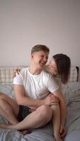 vertical video, young couple sitting on bed, hugging, kissing video