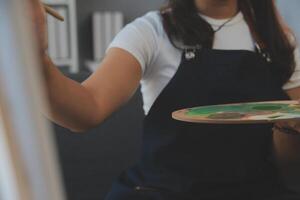 Cropped image of female artist standing in front of an easel and dipping brush into color palette photo