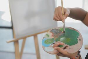 Cropped image of female artist standing in front of an easel and dipping brush into color palette photo