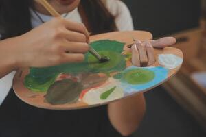 Cropped image of female artist standing in front of an easel and dipping brush into color palette photo