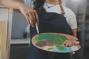 Cropped image of female artist standing in front of an easel and dipping brush into color palette photo