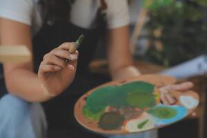 Cropped image of female artist standing in front of an easel and dipping brush into color palette photo