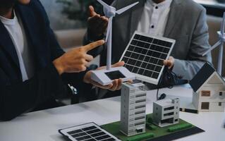Two Young Engineers Expertise in Solar Cell Installation Meetings and Discussion in The Job. Planning to Install Solar Photovoltaic Panels on Roof Top in The Office Room with Factory Building Plan. photo
