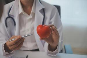 Hands of doctor woman holding red heart, showing symbol of love, human support to patient, promoting medical insurance, early checkup for healthcare, cardiologist help. Close up of object photo