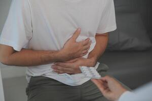 Man suffering with severe stomach pain sitting at home. Hand of mature guy holding abdomen suffering from ache, diarrhea or indigestive problem. Caucasian guy pressing on belly on painful sensation photo