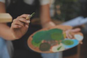 Cropped image of female artist standing in front of an easel and dipping brush into color palette photo