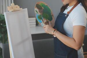 Cropped image of female artist standing in front of an easel and dipping brush into color palette photo