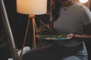 Cropped image of female artist standing in front of an easel and dipping brush into color palette photo