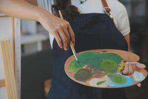 Cropped image of female artist standing in front of an easel and dipping brush into color palette photo
