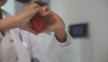 Hands of doctor woman holding red heart, showing symbol of love, human support to patient, promoting medical insurance, early checkup for healthcare, cardiologist help. Close up of object photo