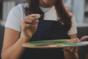 Cropped image of female artist standing in front of an easel and dipping brush into color palette photo