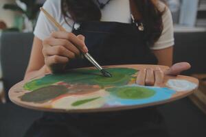 Cropped image of female artist standing in front of an easel and dipping brush into color palette photo