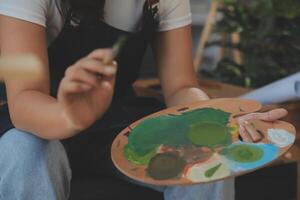 Cropped image of female artist standing in front of an easel and dipping brush into color palette photo