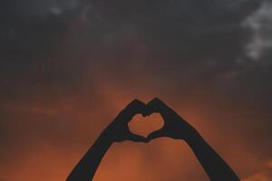 Silhouette of hands in heart symbol around the sun photo