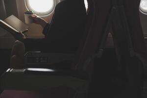 Blonde female tourist checking incoming notification on smartphone sitting on seat of airplane with netbook.Young businesswoman share media from telephone on laptop computer during plane flight photo