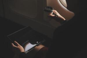 Blonde female tourist checking incoming notification on smartphone sitting on seat of airplane with netbook.Young businesswoman share media from telephone on laptop computer during plane flight photo