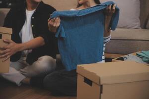 Two Asian blogger showing clothes in front of the camera to recording vlog video live streaming at her shop. Online Shopping Cart notion. on sofa at home photo