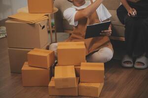 Two Asian blogger showing clothes in front of the camera to recording vlog video live streaming at her shop. Online Shopping Cart notion. on sofa at home photo