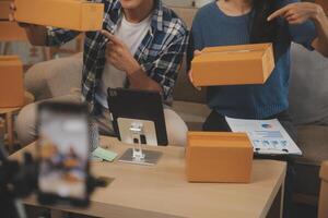 Two Asian blogger showing clothes in front of the camera to recording vlog video live streaming at her shop. Online Shopping Cart notion. on sofa at home photo