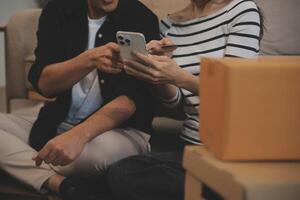 Two Asian blogger showing clothes in front of the camera to recording vlog video live streaming at her shop. Online Shopping Cart notion. on sofa at home photo