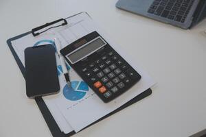 Close up view of simple workspace with laptop, notebooks, coffee cup and tree pot on white table with blurred office room background photo