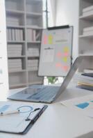 Close up view of simple workspace with laptop, notebooks, coffee cup and tree pot on white table with blurred office room background photo