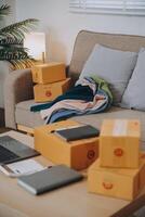 Las pymes asiáticas usan computadoras portátiles para verificar las cajas de envío en línea de pedidos de clientes en casa. Emprendedor de pequeñas empresas pyme freelance. negocio en línea, concepto de trabajo en casa. foto