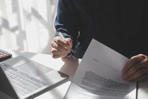Asian businessman reviewing document reports at office workplace with computer laptop. legal expert, professional lawyer reading and checking financial documents or insurance contract photo