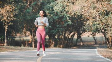 Full body female athlete in activewear running on road path during cardio workout on sunny summer day in park. photo