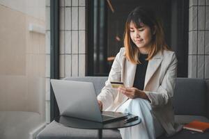 mujer joven con tarjeta de crédito y usando computadora portátil. empresaria trabajando en casa. compras en línea, comercio electrónico, banca por Internet, gastar dinero, trabajar desde el concepto de hogar foto