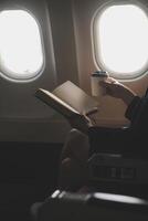 Blonde female tourist checking incoming notification on smartphone sitting on seat of airplane with netbook.Young businesswoman share media from telephone on laptop computer during plane flight photo