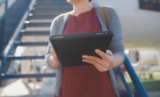 rubia hembra turista comprobación entrante notificación en teléfono inteligente sentado en asiento de avión con netbook.joven mujer de negocios compartir medios de comunicación desde teléfono en ordenador portátil computadora durante avión vuelo foto