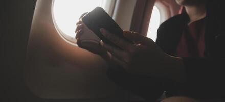 Blonde female tourist checking incoming notification on smartphone sitting on seat of airplane with netbook.Young businesswoman share media from telephone on laptop computer during plane flight photo