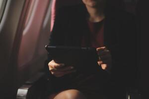 Blonde female tourist checking incoming notification on smartphone sitting on seat of airplane with netbook.Young businesswoman share media from telephone on laptop computer during plane flight photo