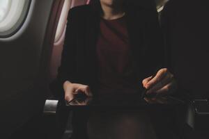 Blonde female tourist checking incoming notification on smartphone sitting on seat of airplane with netbook.Young businesswoman share media from telephone on laptop computer during plane flight photo