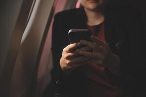 Blonde female tourist checking incoming notification on smartphone sitting on seat of airplane with netbook.Young businesswoman share media from telephone on laptop computer during plane flight photo