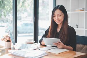 A businesswoman is fully engaged in her work, seamlessly switching between a tablet and a laptop at her organized workspace, symbolizing the dynamic nature of modern professional multitasking. photo