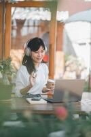 alegre mujer atractivo en un vídeo llamar, disfrutando su café a un iluminado por el sol al aire libre café con su ordenador portátil. foto